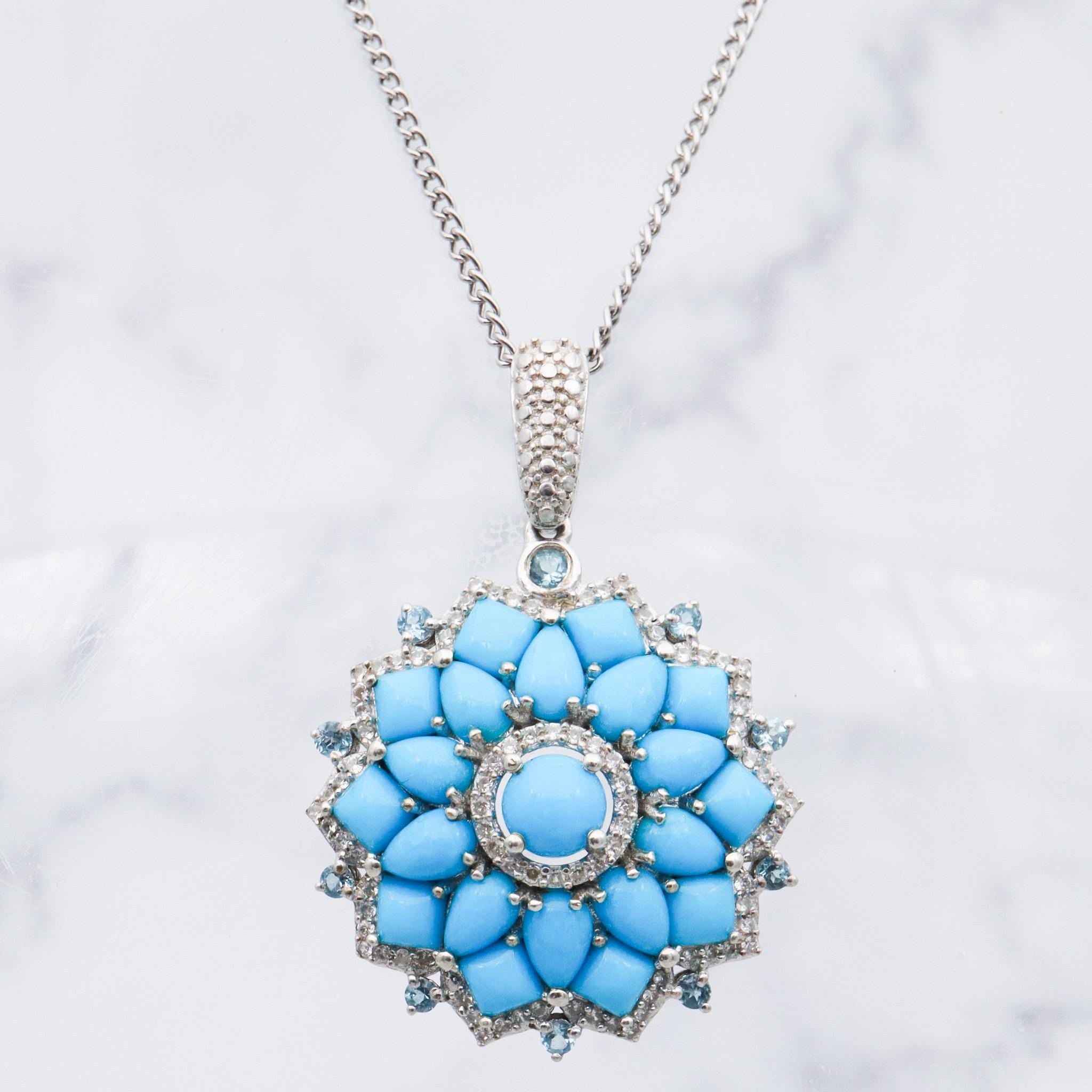 May include: A silver necklace with a blue turquoise flower pendant. The pendant is surrounded by smaller blue stones and silver accents.